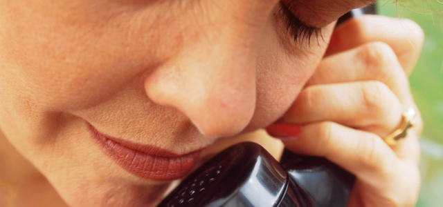 Ältere Dame hält einen schwarzen altmodischen Telefonhörer in der rechten Hand und telefoniert