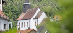 Die Katholische Kirche in Mölschbach steht vor einem grün bewaldeten Berghang.