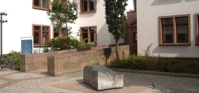 Vor dem Eingang zur Stadtbibliothek, liegt eine große Buchskulptur von ca. einem halben Meter Höhe. Der Buchrücken und die Seiten scheinen 