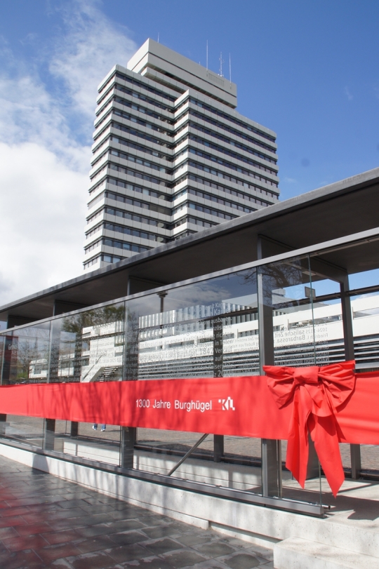 Der neue gläserne Ausgang ist mit einer roten Schleife verpackt. Hinter dem Glasgebäude steht das Rathaus. © PRtext