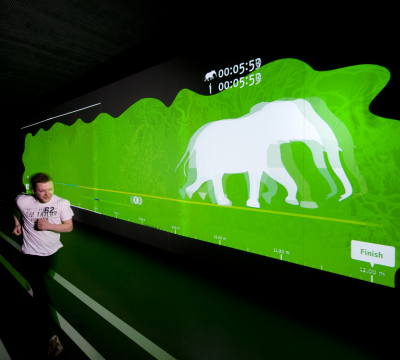 Aufnahme im Wettlauftunnel des Dynamikum in Pirmasens. Ein Mensch läuft gegen einen Elefanten auf der Leinwand.