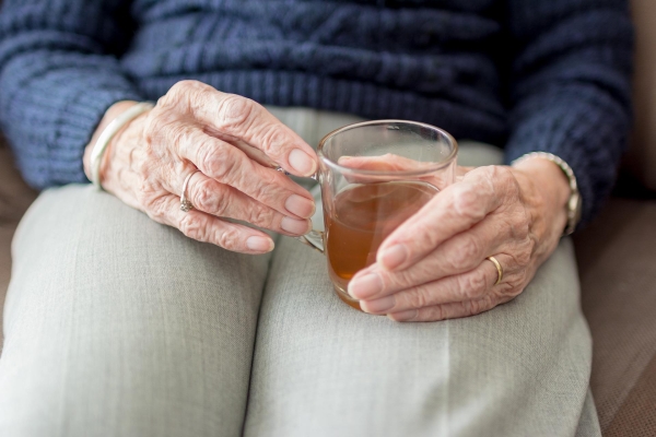 Hand einer alten Frau mit einem Getränk in der Hand.